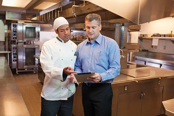 Chef and manager discussing in kitchen.